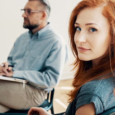 pretty red haired woman in counseling session with male therapist, she is looking at the camera