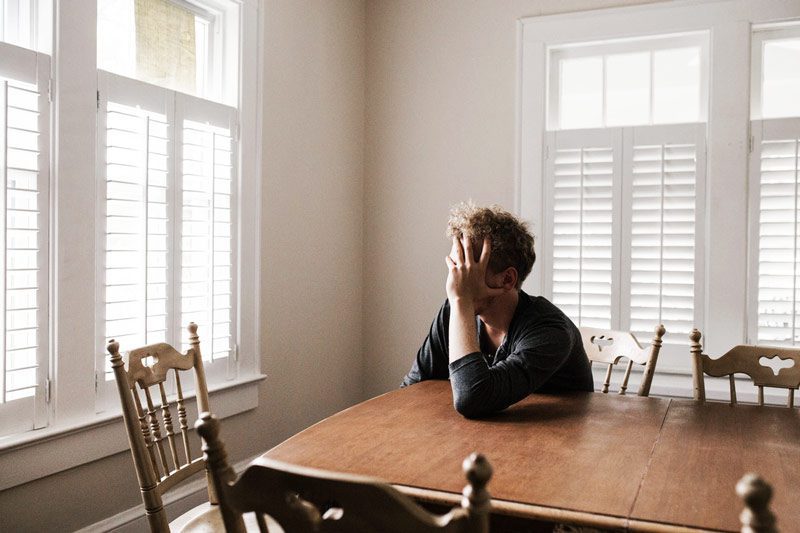 sad man sitting at kitchen table with hand covering his face - seasonal affective disorder - SAD