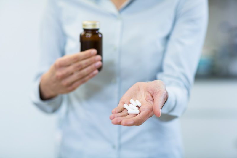 Valium and Xanax Abuse, person who has traded anxiety for euphoria, anxiety or panic disorder, woman holding pill bottle in one hand and white capsules in the other - anxiety, anxiety or panic disorder